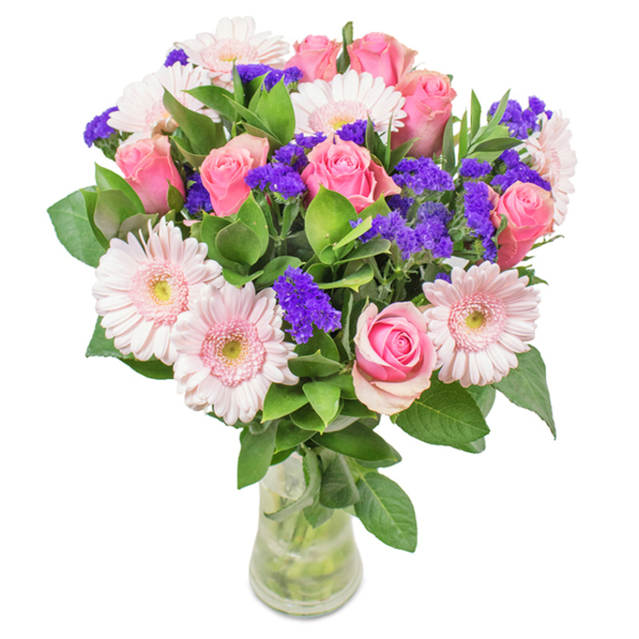 A stunning, elegantly arranged bouquet embodies the refined style of Old Malden Florist, expertly presented in a clear glass vase set against a backdrop of peaceful suburban charm. At its centre, around 7 to 9 perfectly formed soft to medium pink roses catch the eye-some tightly coiled, others just opening to reveal their classic spirals. These are accompanied by 5 to 7 charming pale pink gerbera daisies, their large, round blooms radiating petals around creamy, nearly white centres, imparting a dreamy, airy quality. Scattered throughout are bold patches of vivid purple statice, lending dramatic depth and a unique, textured contrast. The arrangement is richly framed with deep green foliage, reminiscent of Old Malden's established hedgerows and tree-lined streets, enhancing the bouquet's freshness and vitality. The translucent vase, filled with water and visible stems, suggests longevity and the delight of a recent delivery-perhaps destined for a family in The Plough Green area or as a gift celebrating a milestone. This distinctive composition is ideal for birthdays, anniversaries, or as a cherished centerpiece, carrying joy, affection, and a touch of local warmth to any occasion.